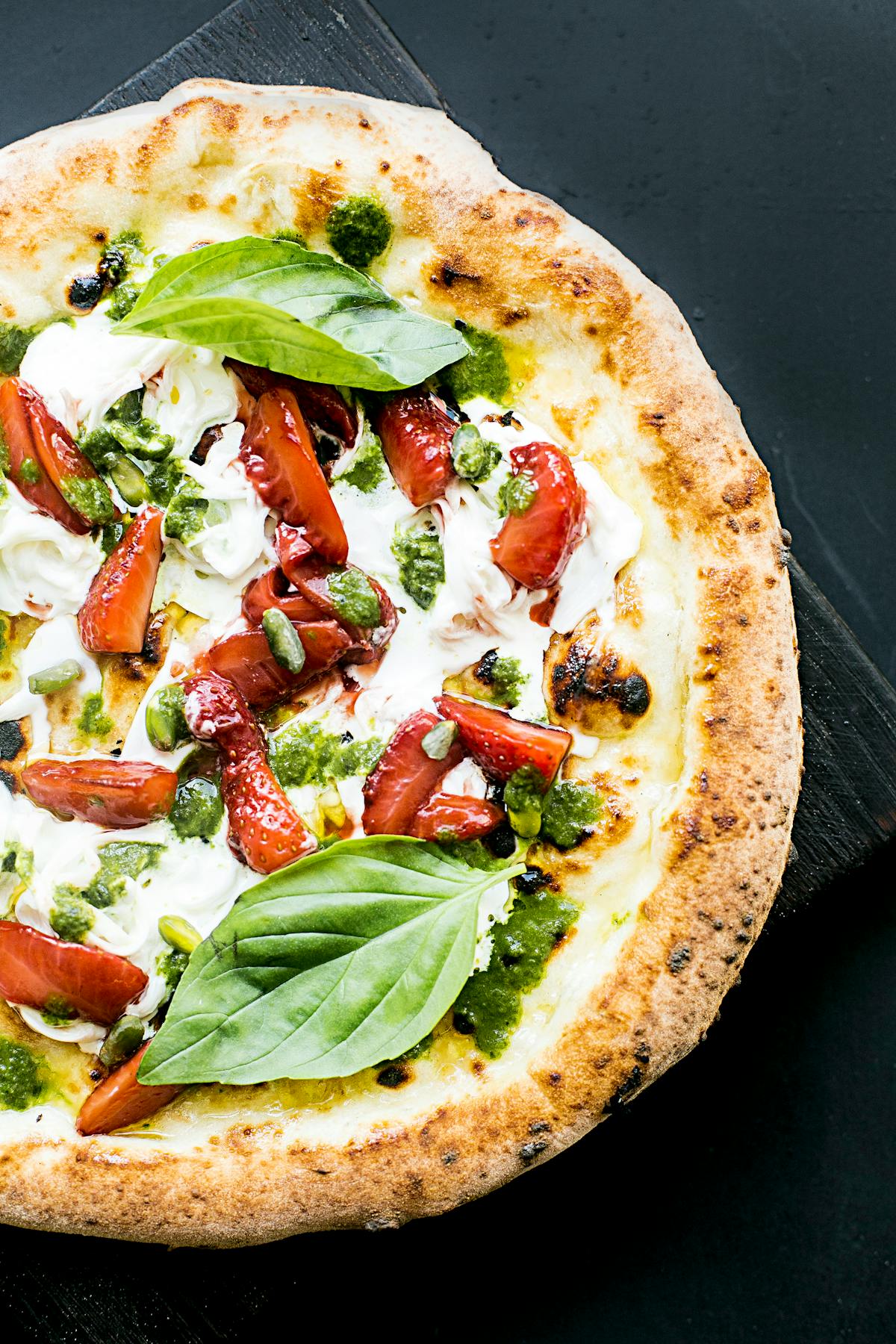 Close-up of a round wood-fired Italian flatbread with a dark-blistered rim, photographed from above on a slate board — illustrative of the oven style used to bake cecìna in Versilia bakeries