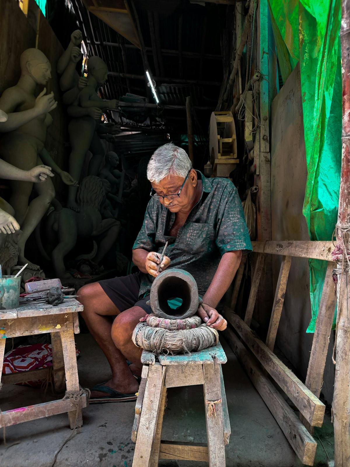 A craftsman in a workshop hollowing out a large sculpted form, surrounded by clay and papier-mâché figures in various stages of construction