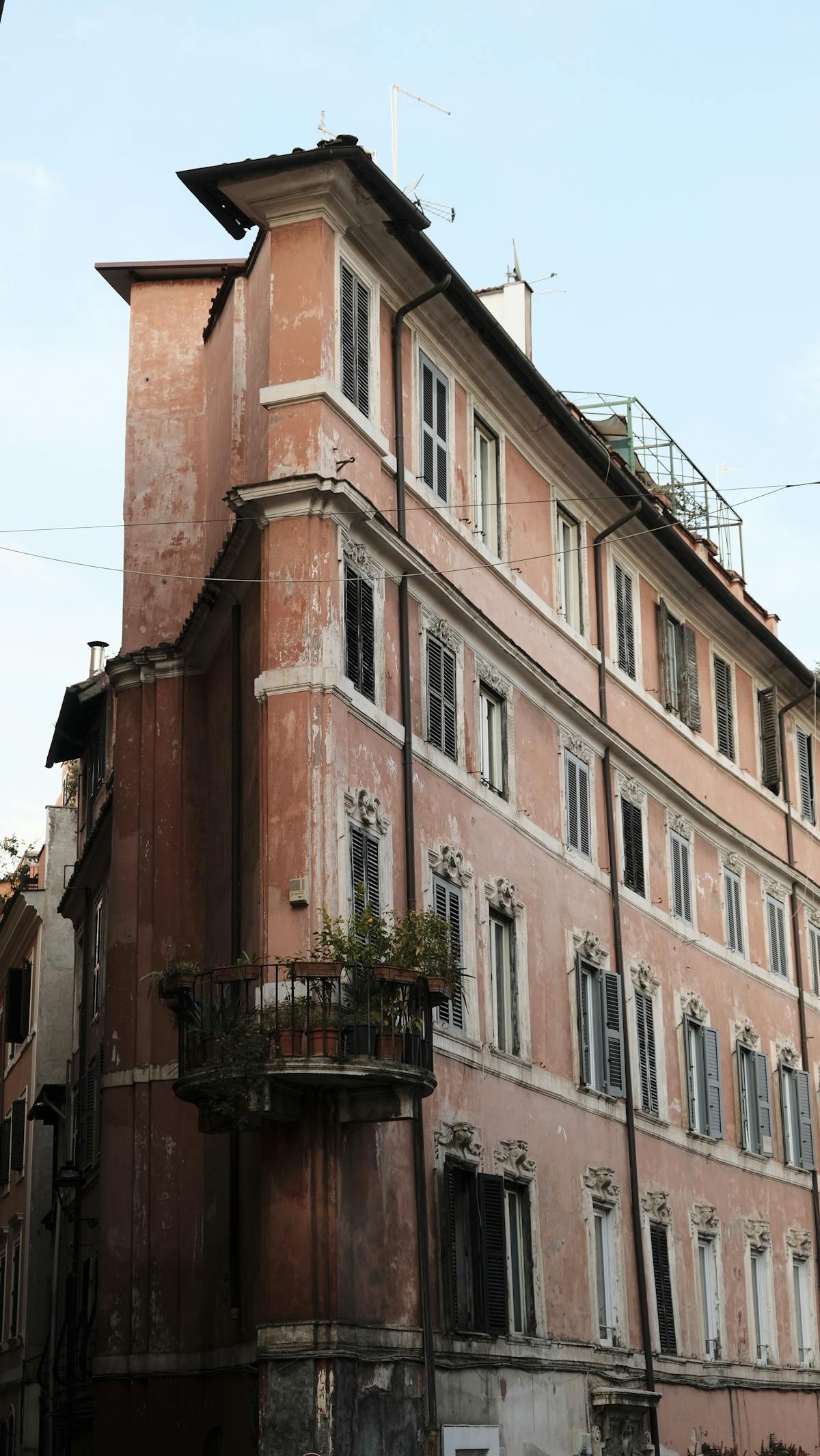 Tall Italian belle-époque facade in weathered pink and ochre, with multi-storey windows and ornamental cornices against a clear sky